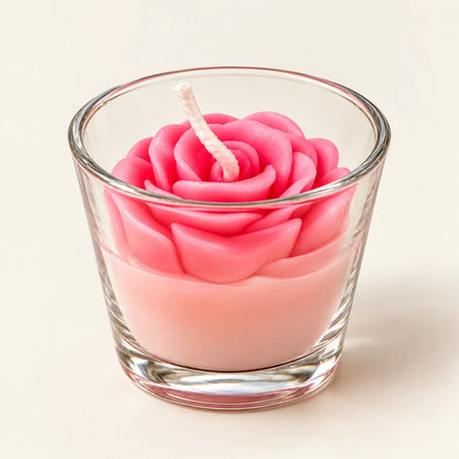 Pink sculpted rose candle inside a transparent glass tumbler on a plain background.